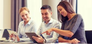 48023817_business-people-and-technology-concept-smiling-business-team-with-tablet-pc-computer-meeting-in-off-e1456525025886